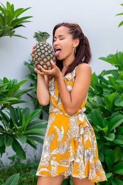 食物身着黄色夏装 手持菠萝的快乐亚洲微笑女人的画像绿色舌头自然