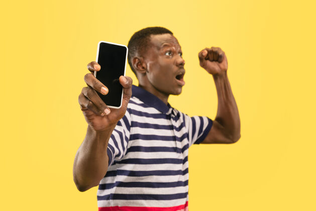 学生年轻的非洲裔美国男子与智能手机隔离在黄色工作室智能手机开朗模特