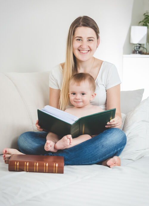 女性快乐的年轻母亲和她的男婴与大书合影的色调肖像小坐着休闲