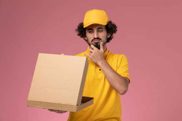 思想正面图身穿黄色制服的男快递员拿着食品快递箱思考着淡粉色的墙壁工人盒子快递