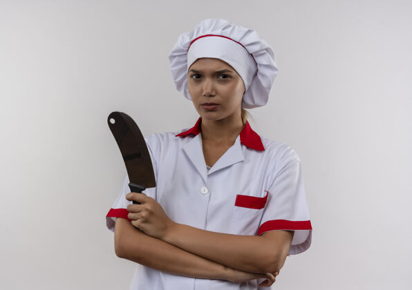 自信自信的年轻女厨师穿着厨师制服双手交叉握着菜刀在隔离的白色墙壁上复制空间交叉劈刀手