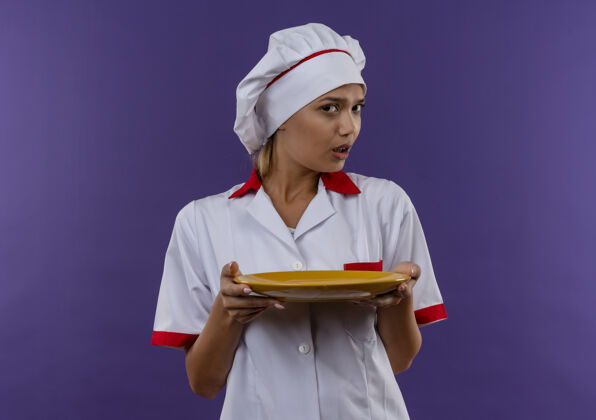 制服困惑的年轻厨师女穿着厨师制服拿着盘子在隔离的墙上复制空间迷糊拿着厨师