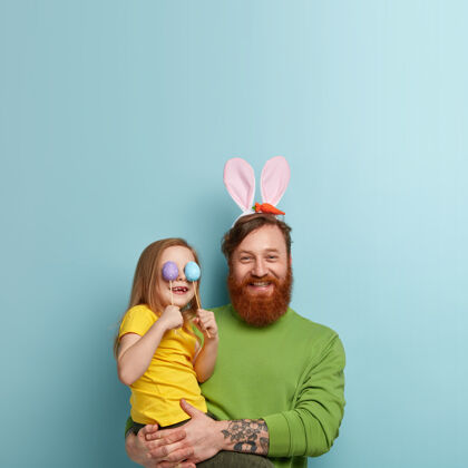人一个留着姜黄色胡子的男人穿着五颜六色的衣服 抱着女儿的兔子耳朵女儿人兔子
