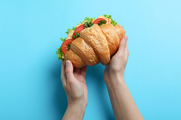 烘焙女性手拿羊角面包三明治在蓝色美味自制房子